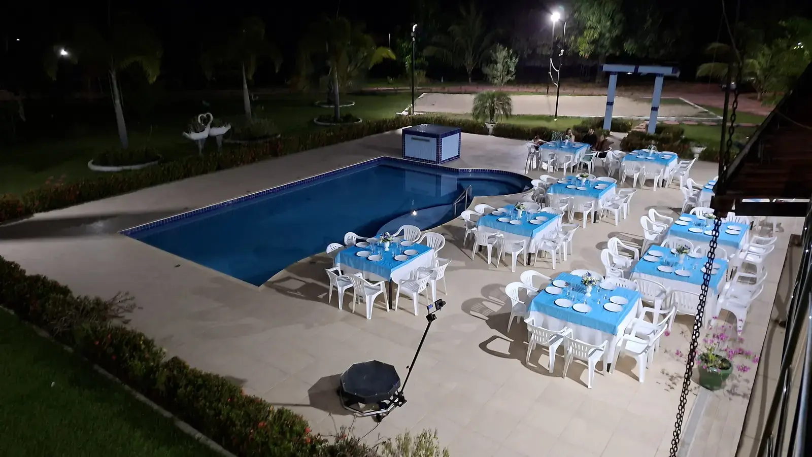Mesas com toalhas azuis montadas em volta da piscina, à noite